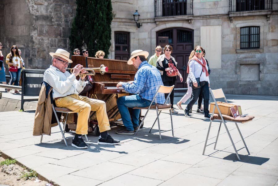 Trumpet and piano player busking outside, with people around.