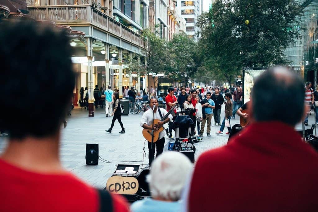 Guitar player playing acoustic guitar outside, around all kinds of people, lots of people.