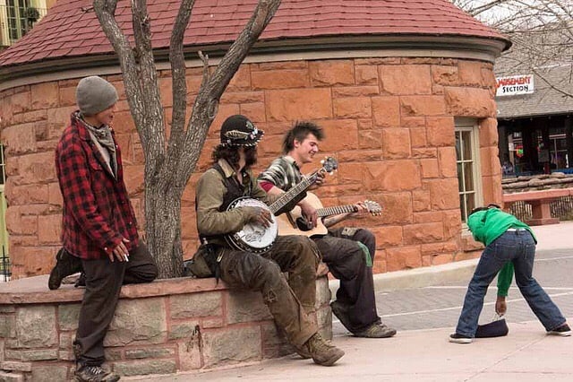 Banjo and guitar player busking outside, with people around, with kid giving money in their container.