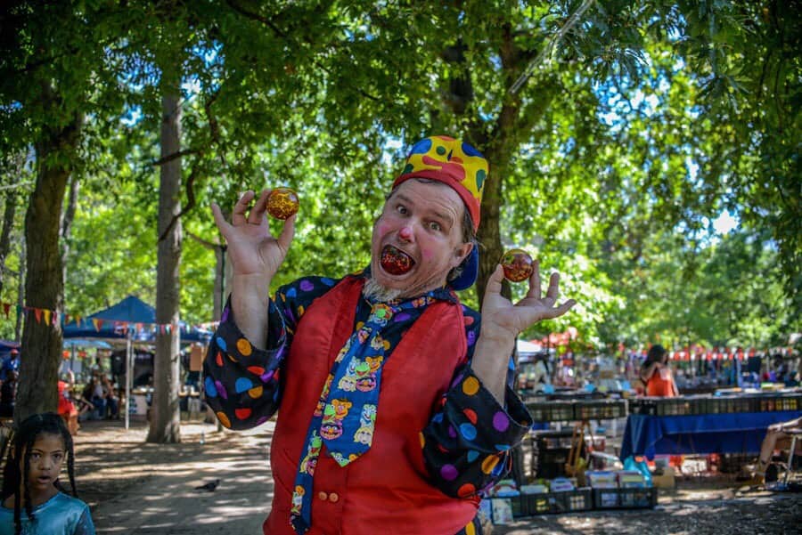 Juggler with balls in his hand and mouth, outside, smiling and acting clown like.