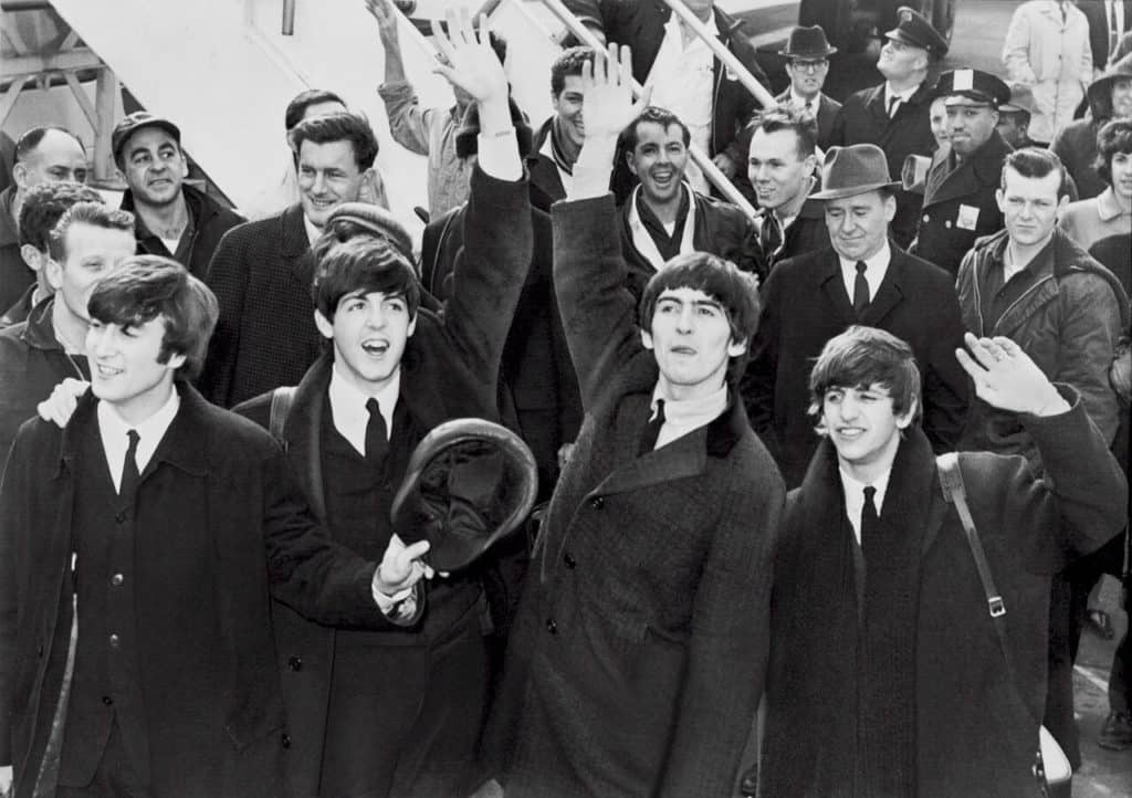 The Beatles wave to fans and media. The Beatles black and white picture photo in public domain from commons.m.wikimedia.org