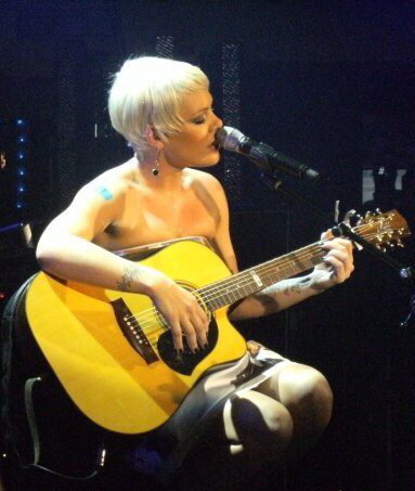 Pink playing guitar on stage, sitting down. Photo courtesy of Corbuzon. commons.m.wikimedia.org