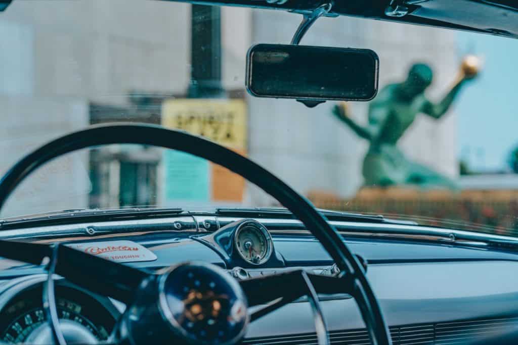 Inside of car, with statue of juggler, to the right of it, outside of car.