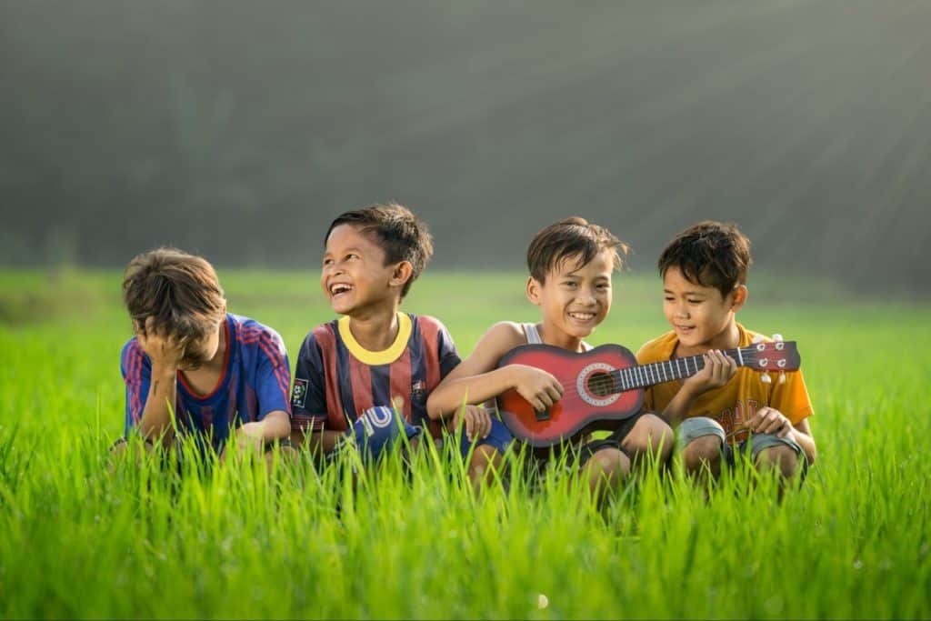 Kids around a kid playing ukulele, all kids having lots of fun.