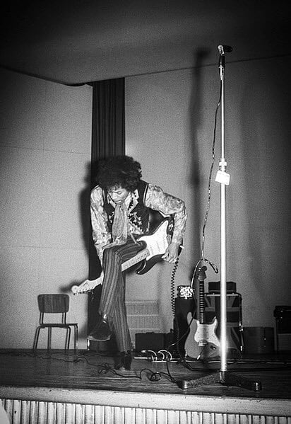 Jimi Hendrix playing guitar between his knees, on stage. Black and white picture.