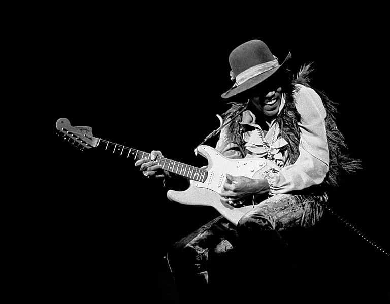 Jimi Hendrix smiling and playing guitar, while bending his knees. Black and white picture.