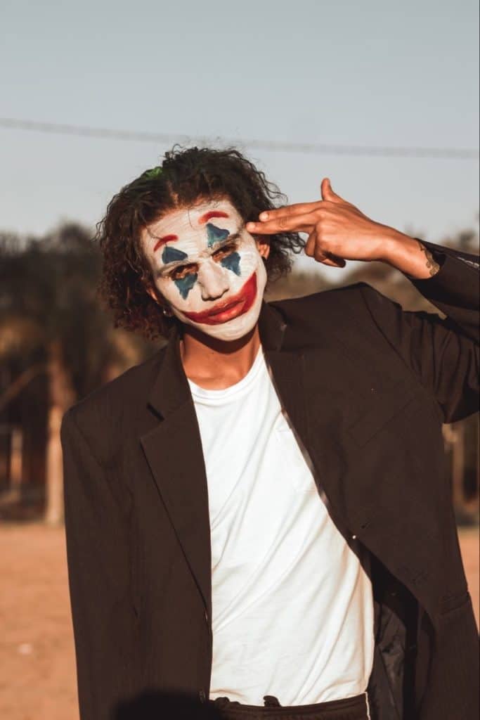 Joker clown pointing to his face using two fingers.