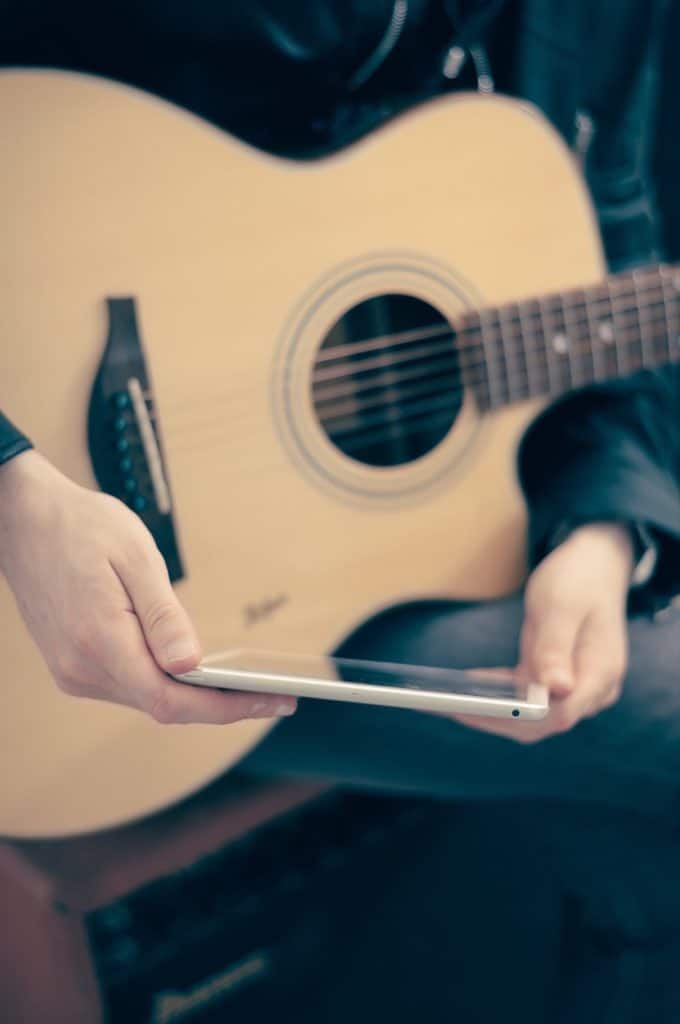 Man using iPad and playing acoustic guitar.