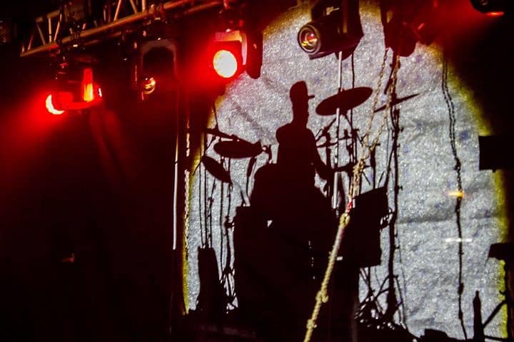 Shadow of drummer playing drums on lighted stage. 